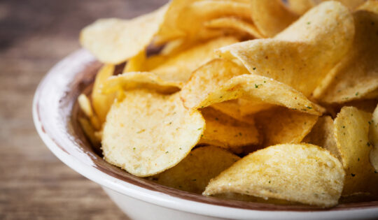 heap of potato chips in bowl on wooden background
